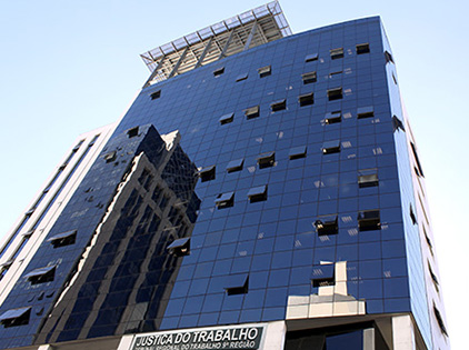 A imagem mostra a fachada da sede do TRT-PR, na Rua Carlos de Carvalho, 528. A foto foi tirada de baixo e possibilita ver uma pequena parte a lateral do prédio.