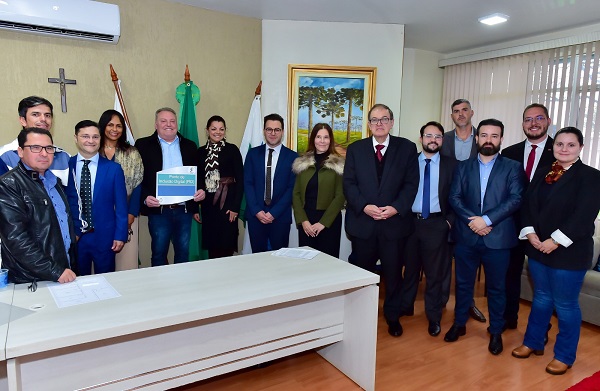 Fotografia com 14 pessoas no gabinete do prefeito de Coronel Domingos Soares. O prefeito segura a placa do PID ladeado por servidores e autoridades locais.