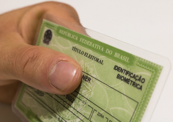 Fotografia da mão de uma pessoa mão segurando o título do eleitor brasileiro. No documento, está escrito República Federativa do Brasil, título de eleitor.