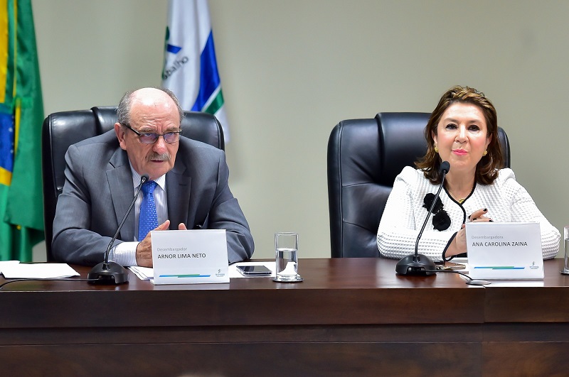 Fotografia do ouvidor do TRT-PR, desembargador Arnor Lima Neto, vestino de terno cinza com gravata azul, homem calvo, fala ao microfone em frente a uma mesa; ao lado da diretora da Escola Judicial, desembargadora Ana Carolna Zaina, mulher branca de cabelos até altura do ombo, veste blusa branca.