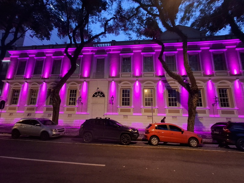 Fachada do prédio histórico na sede do TRT-PR, em Curitiba, com luzes na cor rosa projetada sobre as paredes.