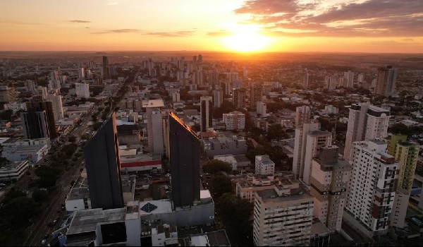 Fotografia aérea do pôr do Sol em Cascavel, com destaque para as linhas de avenidas na cidade e o aglomerrado de prédios.