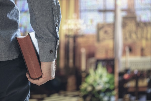 Homem de pele clara segurando bíblia sagrada na igreja com altar em segundo plano.