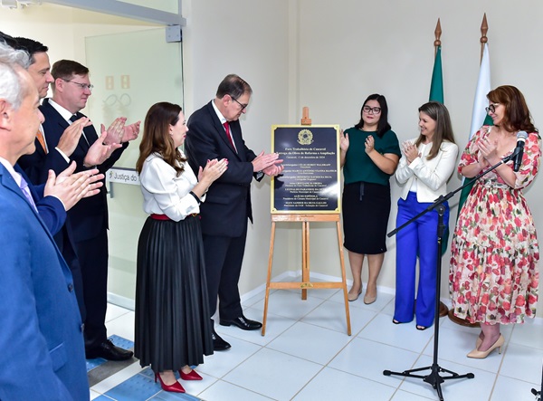 Fotografia do momento da inauguração da placa que marca a reforma do prédio do Fórum Trabalhista de Cascavel. A placa está ao centro e ao lado dela diversas pessoas, entre homens e mulheres, aplaudem o momento. 