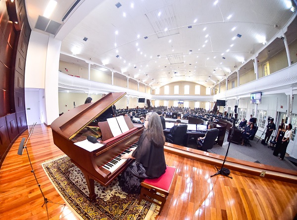 Fotografia com lente olho de peixe mostra uma mulher tocando piano no palco do plenário Pedro Ribeiro Tavares.