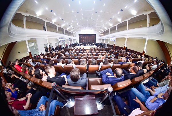 Fotografia com lente olho de peixe (que distorce as bordas) mostra o plenário Pedro Ribeiro Tavares lotado com a plateia de costas. Ao fundo, a mesa de autoridades na abertura do evento.