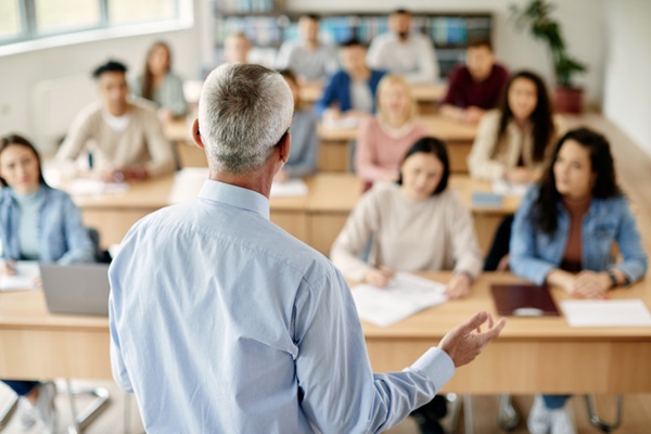 Visão traseira do professor dando palestra para grande grupo de estudantes da universidade.