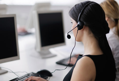 imagem fechada mostra perfil de uma teleatendente usando um headphone à frente de uma tela de computador