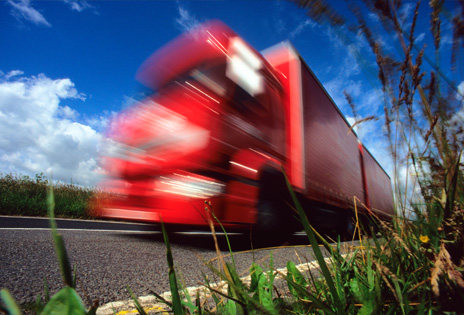 imagem capturada à margem de uma rodovia mostra um caminhão passando, com efeito de desfoque dando a sensação de velocidade